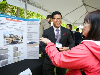 A student and a person talking about an undergraduate project while standing in front of the project's pamphlet.